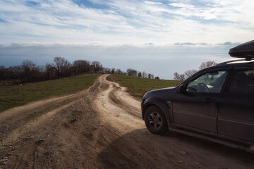Fototapeta na wymiar A gravel road leading toward horizon. Spectacular view on the sea and blue sky in the evening. Offroad 4x4 car