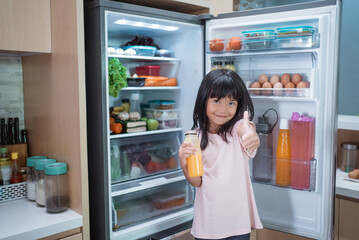 happy young asian girl open fridge door drinking a bottle of juice