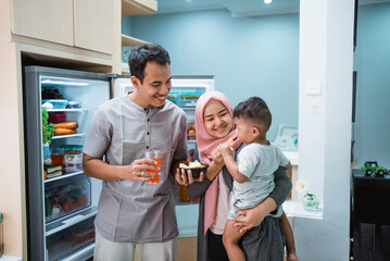 happy young muslim family having iftar breaking the fast while standing in the kitchen eating dates fruit