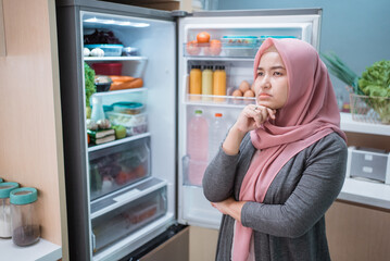 muslim asian woman thinking while open the refrigerator door before cooking in the kitchen