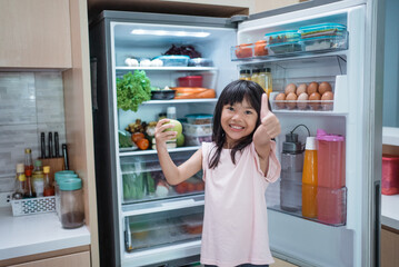 happy young asian girl open fridge door drinking a bottle of juice