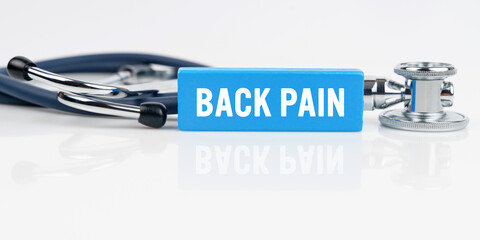 On a white reflective surface is a stethoscope and a blue Jenga with the inscription - BACK PAIN