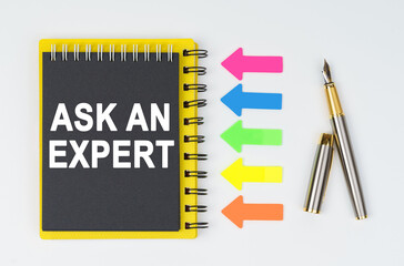 On a white background lies a pen, arrows and a notebook with the inscription - ASK AN EXPERT