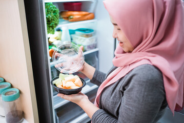 Fototapeta na wymiar muslim woman taking some fruit out of the fridge and eat, dieting concept
