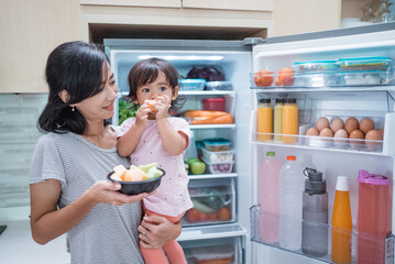 mother carrying her toddler baby and eat fruit together in the kitchen