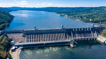 Aerial photography. Bird's eye view of the Krasnoyarsk Hydroelectric Power Plant. A powerful dam blocking the Yenisei River. Depicted on a 10 ruble bill of Russia. Mountains and green mountain taiga