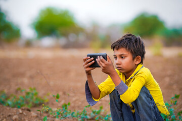 Indian poor child playing with mobile at agriculture field. Rural scene.