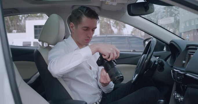 Man with camera sitting inside car and making photo with professional camera, private detective or paparazzi spying.