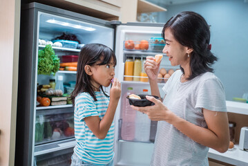 asian mother and her daughter having snack time together in the kitchen open the fridge shoot from inside