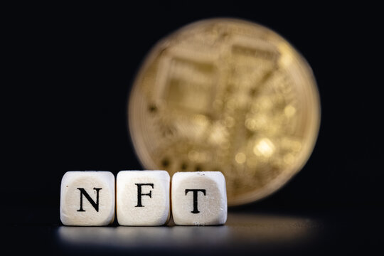 A NFT (non-fungible token) is a special crypto token that uses blockchain technology to link with a unique digital asset. The word NFT is laid out of cubes with letters on background golden cryptocoin