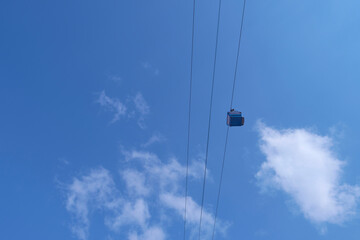 Funiculars on suspended cables move uphill against the background of a blue sky with clouds.
