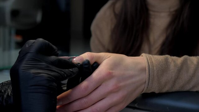 Professional manicurist in black sterile gloves colours fingernail with gel under electric light. Concept design