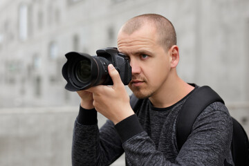 handsome male photographer taking photo with modern dslr camera over concrete building background