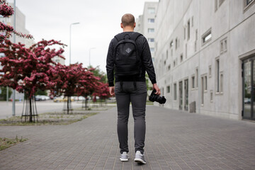 photography and creativity concept - back view of male photographer with modern dslr camera walking in modern city