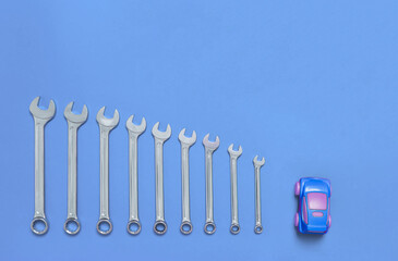 Set of wrenches different size and small toy car lays on a blue background. Banner with tools of locksmith for car service and tire fitting with industrial concept. Close-up.