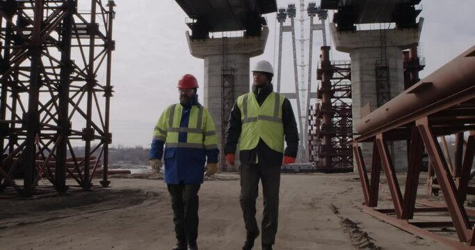 Male Builders Walking Under Bridge