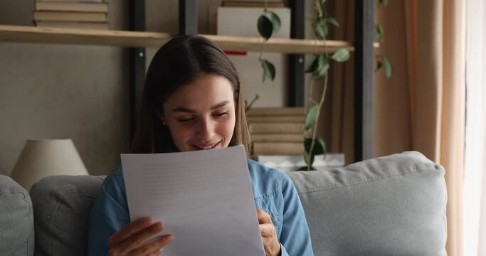 Attractive woman sit on couch holding sheet read letter receiving celebrate good news concept. Student read about abroad internship invitation, bank loan approved, bank statement and financial success