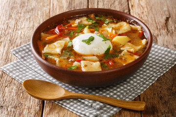 Delicious Pancutras or Pantrucas soup with vegetables, ground beef, noodles and poached egg close-up in a bowl on the table. horizontal
