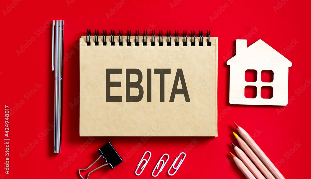 Poster ebita text writtenon red background on a notebook with pencils and office tools and model wooden hou
