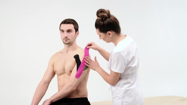 The doctor glues a special treatment tape to mail shoulder. Physiotherapist sticks kinesio tapes to the shoulder of patient, kinesiology taping, kinesiological therapy, athlete are recovering after
