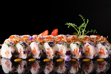 Set of bright sushi rolls on a dark background with flowers and sauce.