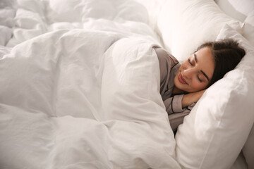 Beautiful young woman wrapped with soft blanket sleeping in bed at home - Powered by Adobe