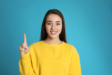 Woman showing number one with her hand on light blue background