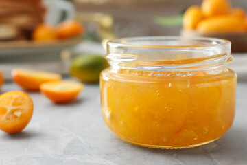 Delicious kumquat jam in jar on light grey marble table, closeup