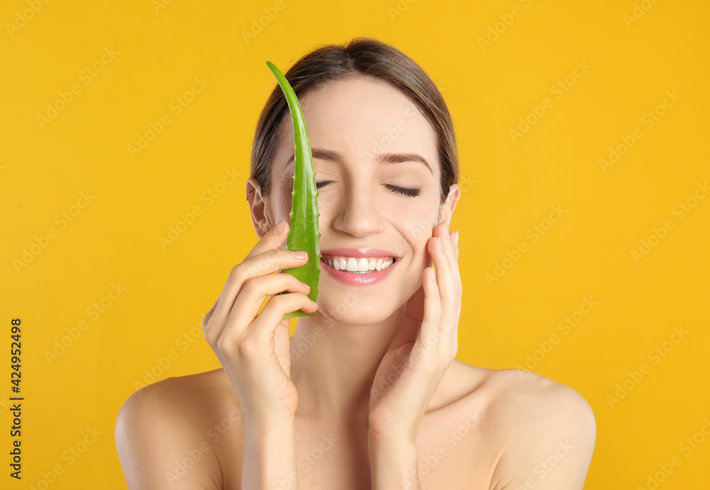 Wall mural Happy young woman with aloe leaf on yellow background