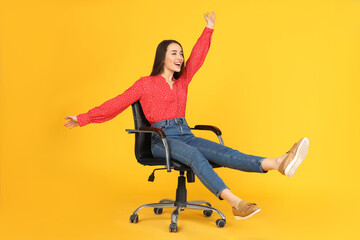 Young woman riding office chair on yellow background