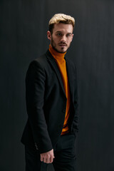 sexy blond guy in dark clothes and orange sweater cropped view black background