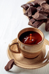 Hot chocolate and broken pieces of bitter chocolate on a white wooden table.