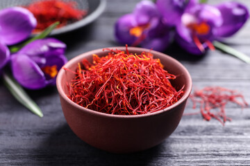 Dried saffron in bowl and crocus flowers on black wooden table, closeup