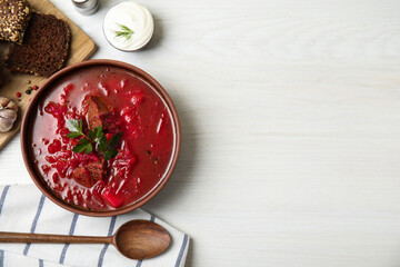 Stylish brown clay bowl with Ukrainian borsch served on white wooden table, flat lay. Space for text