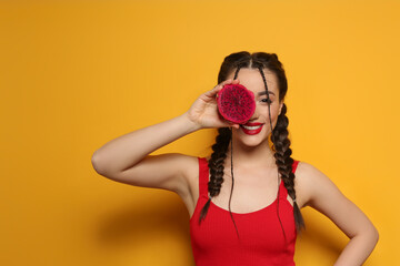 Young woman with fresh pitahaya on yellow background, space for text. Exotic fruit