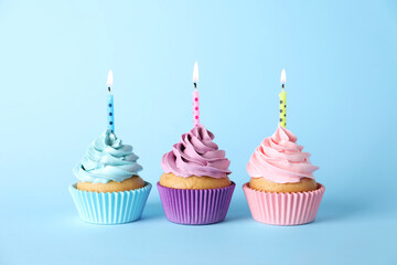 Delicious birthday cupcakes with burning candles on light blue background