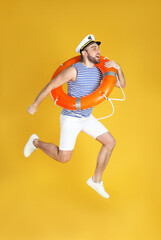Emotional sailor with ring buoy jumping on yellow background