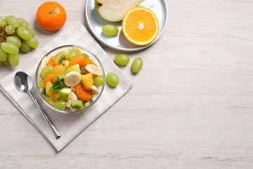 Delicious fresh fruit salad in bowl on white wooden table, flat lay. Space for text