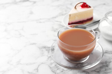 Delicious tea with milk in glass cup near dessert on white marble table. Space for text
