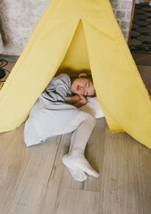 a little tired girl sleeps on the floor after playing in a yellow teepee