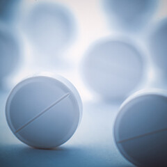 A pile of white pills scattered on a white background with blue tinting. Selective focus.