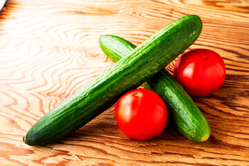 two cucumbers and two tomatoes on a wooden surface