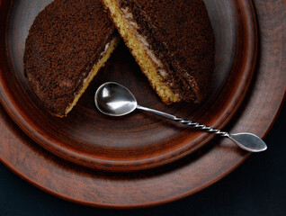 A tiramisu cake with a silver spoon on a clay plate. Top view.