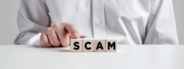 Man pressing his finger on the wooden cubes with the word scam.