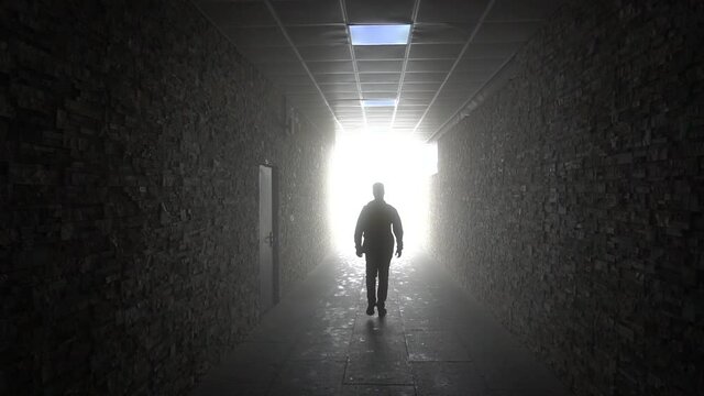 Light at the end of the tunnel. The dark silhouette of a man moves. Corridor with bright light. Stone walls and floor. Shadow of a man on the floor. Mysticism.