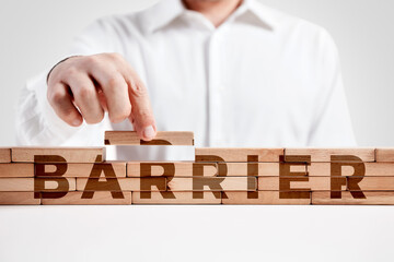 Businessman builds a structure of wooden blocks with the word barrier. Building a barrier
