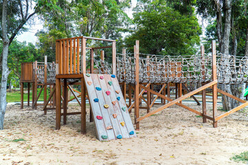 Fototapeta na wymiar Wood playground with climbing rock ladder in the garden background. Wooden panel playground with stone simulation in the park