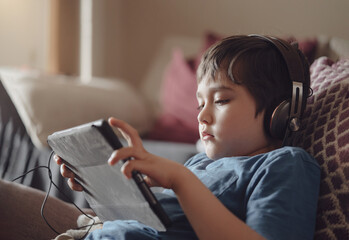 Authentic portrait Kid sitting on sofa watching cartoons on tablet,Yong boy playing game on touch...