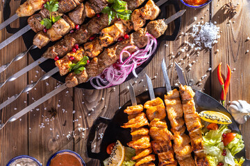 Minced kebab on a metal skewer with sauce, sliced cucumbers, tomatoes and onions.