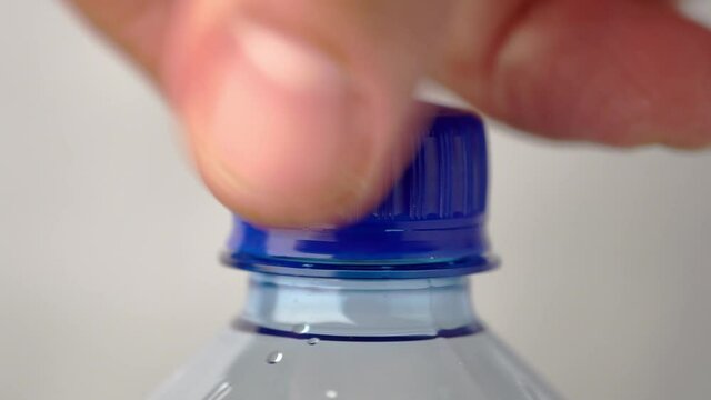 Male hand unscrews and screws cap of a new plastic bottle of carbonated water close up